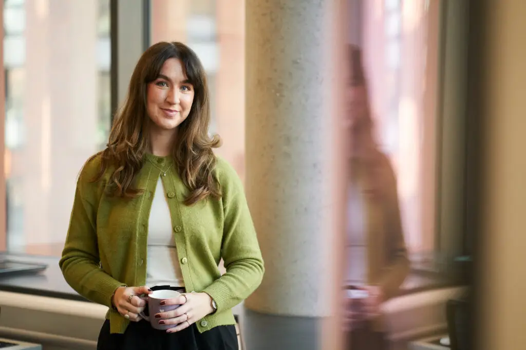 Emily, MacMartin's copywriter, smiling at the camera holding a mug in a city office.
